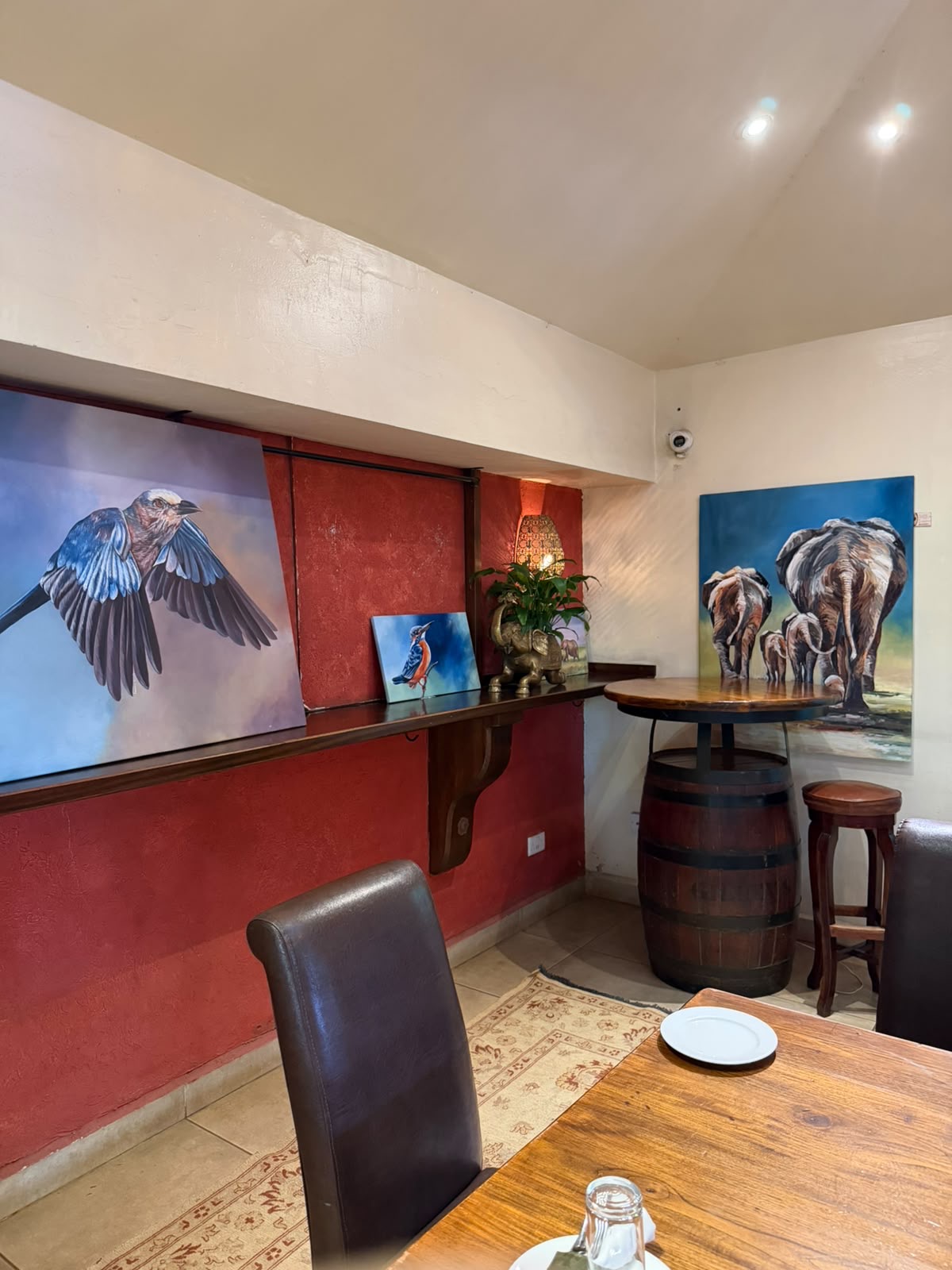 Bird and elephant canvases hung along the red dining room wall