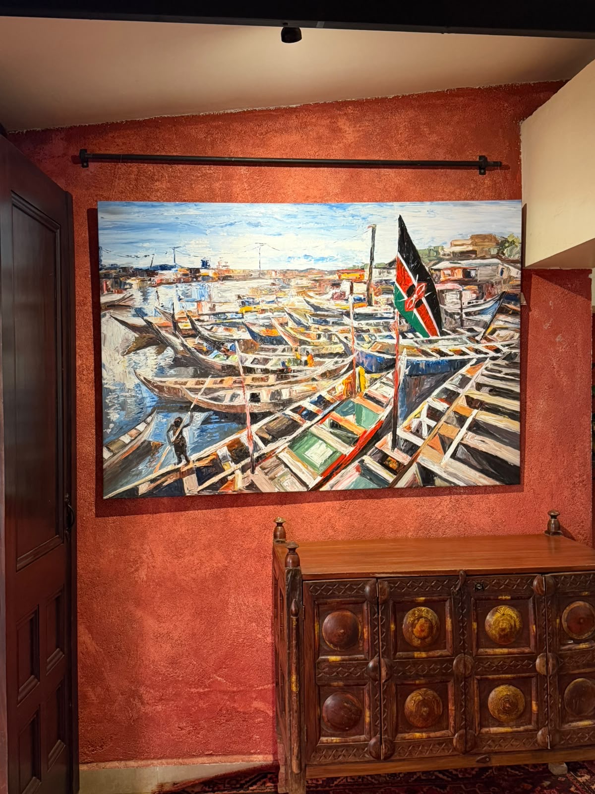 A large oil painting of dhows and a Kenyan flag, hung above a carved chest